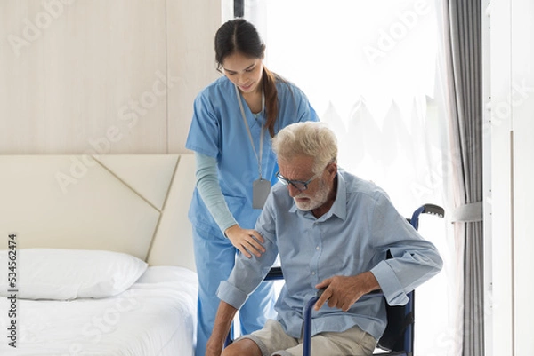 Fototapeta Young asian female nurse and patient senior man. Female nurse caring old man walk from wheelchair at hospital ward. Nurse helping elderly man walk from wheelchair at nursing home