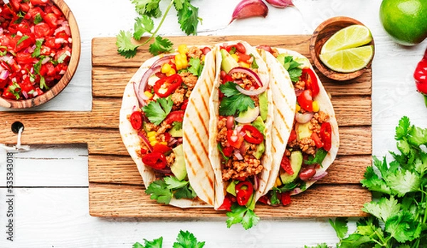 Obraz Mexican cuisine. Tacos with beef, corn, red beans, tomato salsa sauce and onions in corn tortilla on board. White table background, top view