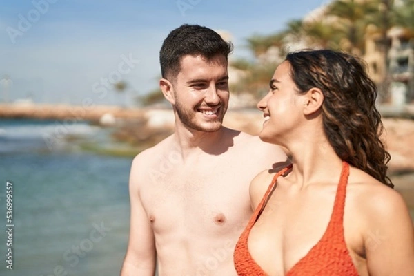 Fototapeta Young hispanic couple tourists wearing swimsuit hugging each other at seaside