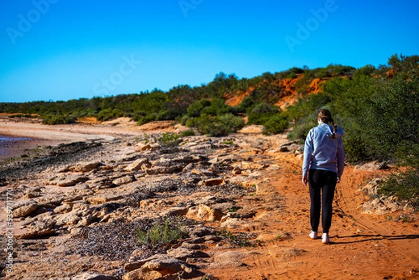 Fototapeta girl walks on red sand beach with red cliffs in the background, terra rosa in australia, holidays in western australia, francois peron national park