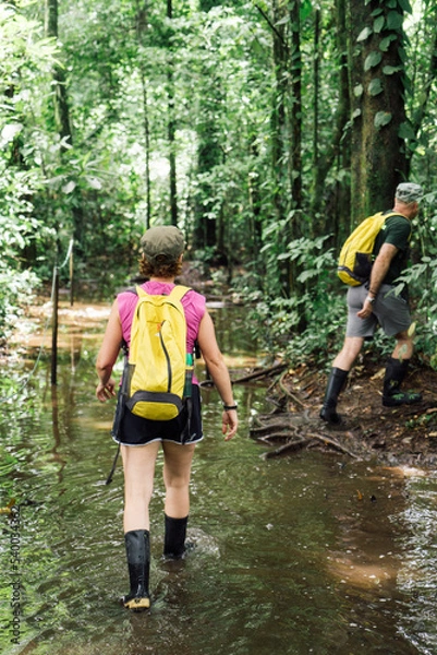 Fototapeta Couple wearing high boots crossing rivers within a tropical jungle in Costa Rica.