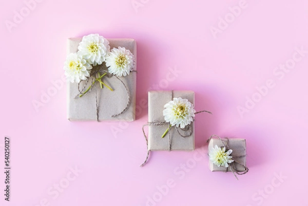 Fototapeta Three gift boxes in gray craft paper decorated with white dahlia flowers on a pink background for the holiday.