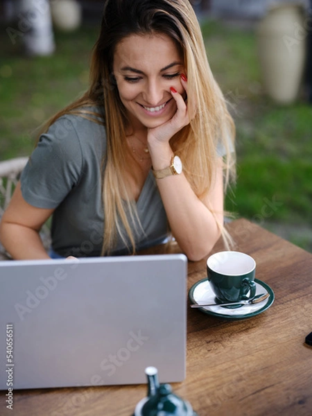 Fototapeta A woman sits in a coffee shop and follows online course.