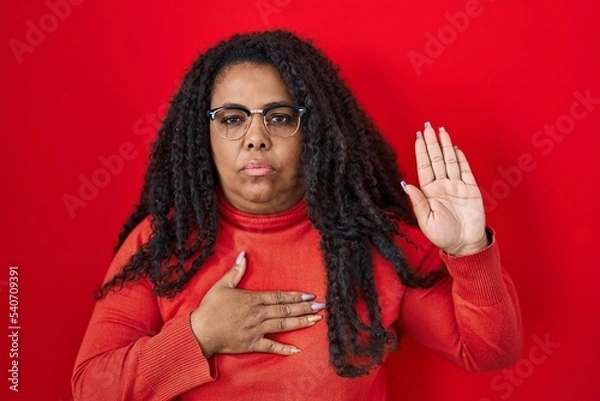 Fototapeta Plus size hispanic woman standing over red background swearing with hand on chest and open palm, making a loyalty promise oath