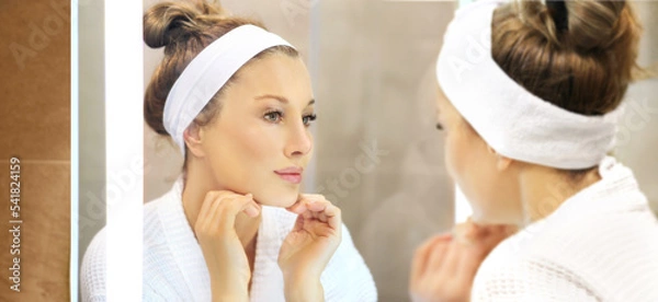 Obraz woman looking in the mirror in the bathroom and taking care of her skin.Applying the cream	.Magic anti-aging cream.