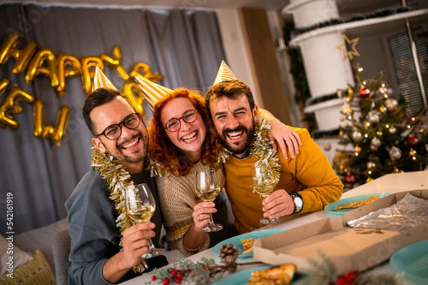 Fototapeta Young people looking at the camera smiling and laughing at the new year's party drinking wine and champagne.