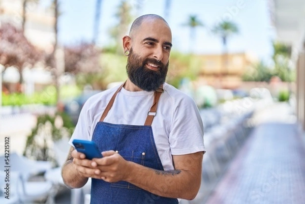 Obraz Young bald man waiter smiling confident using smartphone at street