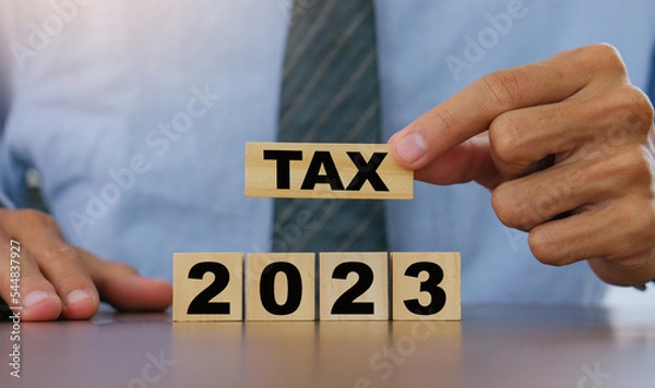 Obraz TAX in 2023 concept,Business man holding wooden block. State taxes,tax payment, governant ,finance, tax accounting, statistics and ,tax return, strategy plan, report.new year concept.