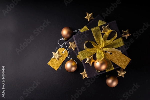 Fototapeta Merry Christmas Happy Holidays greeting card background, New Year, Noel, Winter xmas holidays flat lay. Christmas golden ornaments, decor fir tree, gift boxes on black background top view copy space