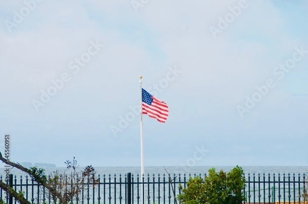 Fototapeta American flag flying with pacific ocean and blue sky background