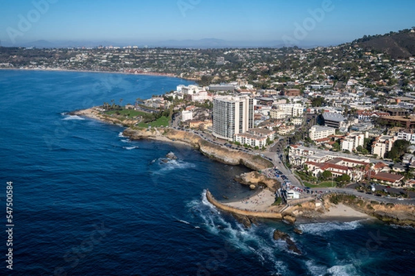 Fototapeta Aerial image of Children's Pool by Seal Rock in La Jolla San Diego California with mountains in the background and palm tree lined roads