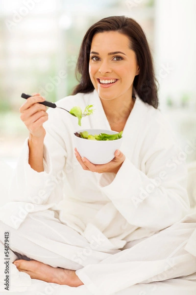 Fototapeta woman sitting on bed eating green salad