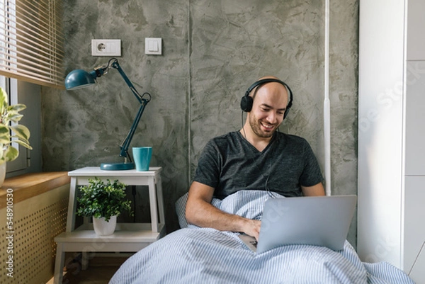 Fototapeta Man working from home, using laptop in bed