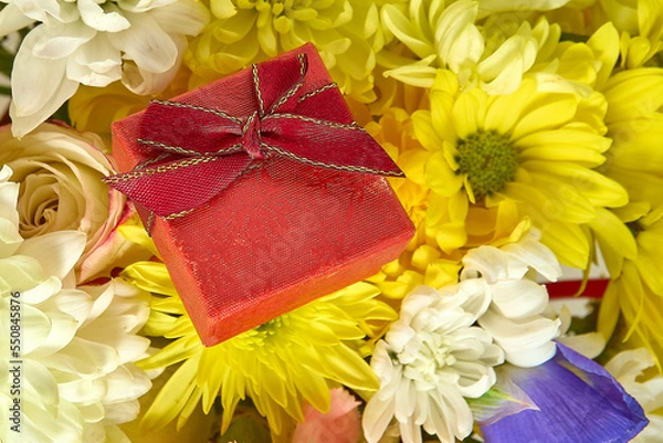 Fototapeta Red jewelry gift box on a bouquet of yellow and white flowers close-up. Top view