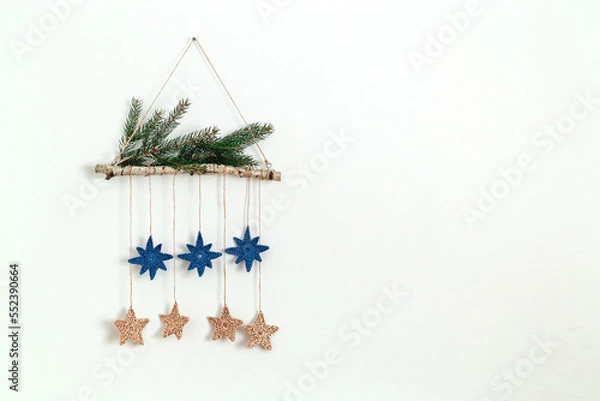 Fototapeta Christmas eco decor made of birch stick, crocheted blue and beige stars and fir tree branches hanging on the white wall. Alternative Christmas. Zero waste holidays. Copy space.