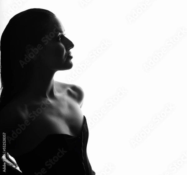 Fototapeta Beautiful and sexy woman silhouette with black corset and wet hair in bright glowing studio background. Model standing in grace pose and looking aside camera with seductive look. Black and white image