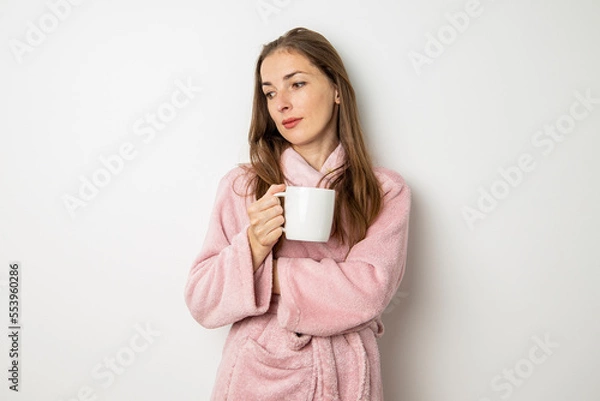 Fototapeta Young woman in a bathrobe drinks coffee on a white background