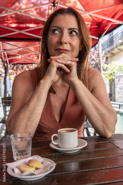 Fototapeta Attractive adult female sitting at coffee table outside waiting for her date. Vertical.