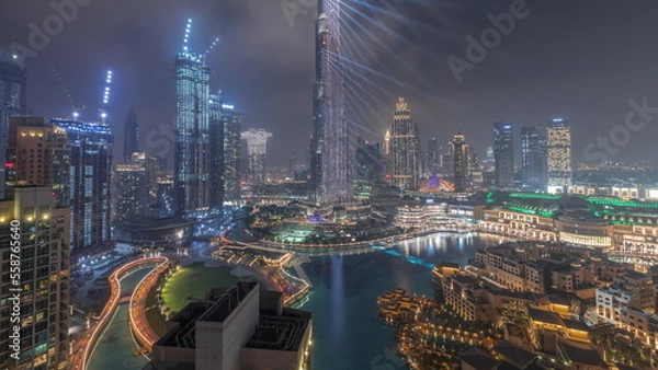 Fototapeta Skyscrapers rising above Dubai downtown all night timelapse surrounded by modern buildings aerial top view