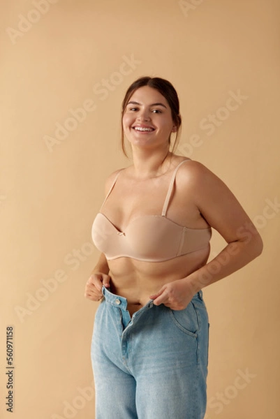 Fototapeta Plus Size Woman in Jeans. Overweight Smiling Woman Demonstrating Weight Loss. Happy Girl Showing Large Jeans And Looking At Camera 