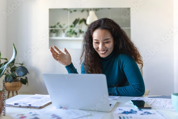 Fototapeta Asian businesswoman on a video call while sitting at her desk. Shot of an attractive young woman using her laptop to make a video call at home