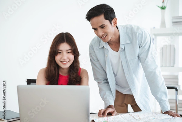 Fototapeta Travel concept, Happy Asian young couple using a laptop to find the location for travel and book hotel online, prepare to travel