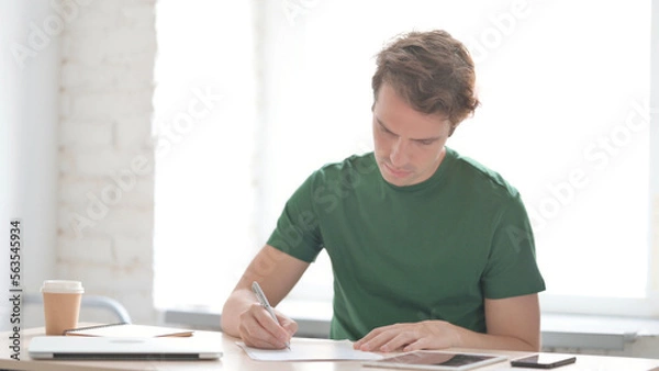 Fototapeta Young Man Writing on Paper in Office