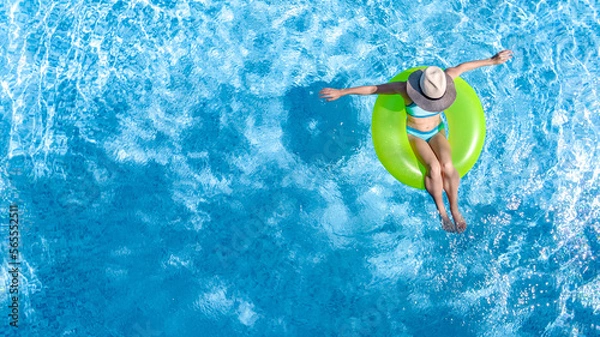 Obraz Active young girl in swimming pool aerial top view from above, teenager relaxes and swims on inflatable ring donut and has fun in water on family vacation, tropical holiday resort
