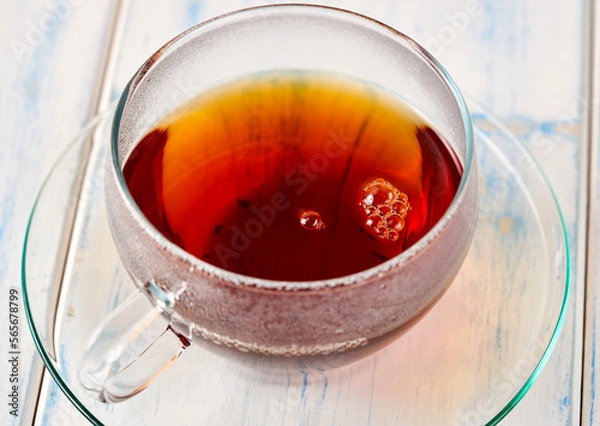 Fototapeta Black tea in a glass mug on a white wooden table.