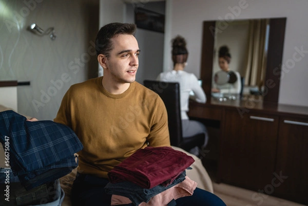 Fototapeta Man caucasian couple packing or unpack wardrobe cloth from suitcase at hotel room while his wife or girlfriend sit in background travel and vacation concept copy space