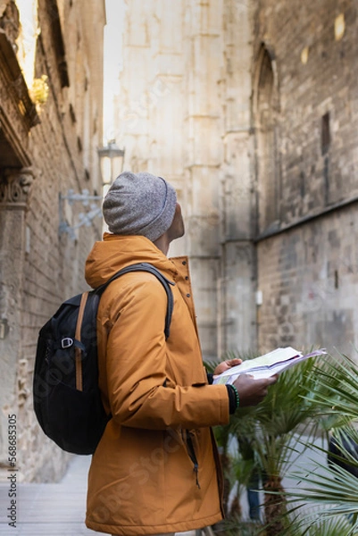 Fototapeta Young girl on vacation with winter clothes and map visiting the gothic quarter of Barcelona (Spain).