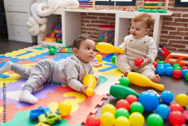 Fototapeta Two adorable babies playing with balls and bowling pin sitting on floor at kindergarten