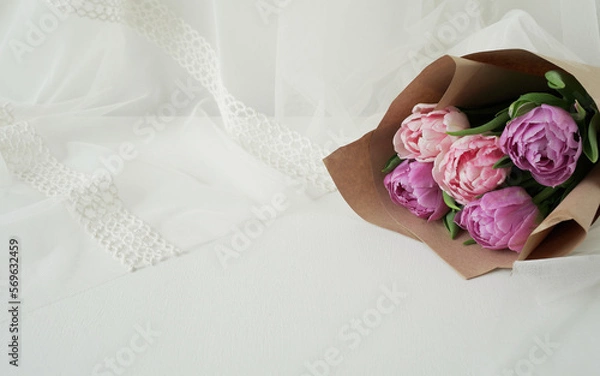 Fototapeta bouquet of exquisite varietal tulips on a gentle light background. flowers in kraft paper on a fabric background.