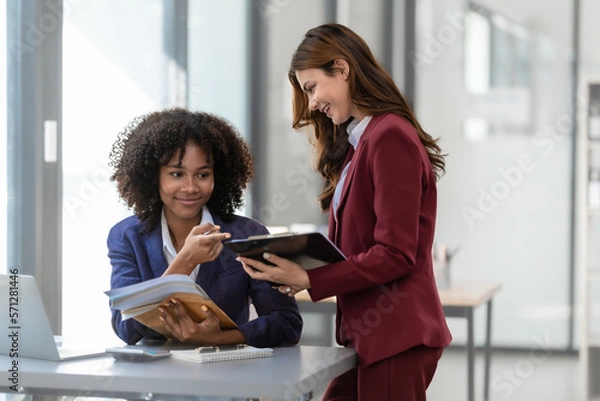 Fototapeta Young trader mixed race woman in formal suit friends consulting and discussing with stock market and cryptocurrency in online trading application.