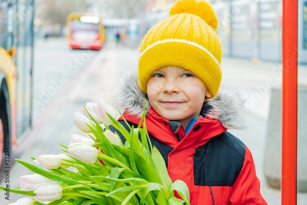 Fototapeta Beautiful boy on city street near bus stop with bouquet of tulips in his hands..