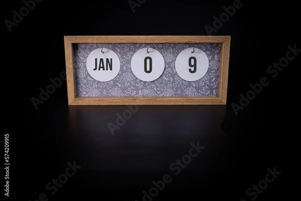 Fototapeta A wooden calendar block showing the date January 9th on a dark black background