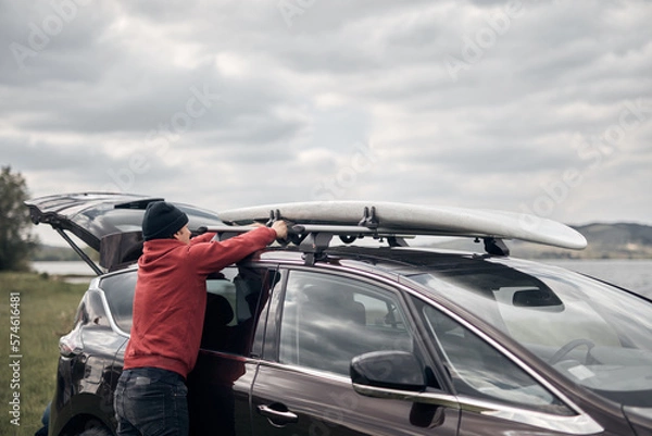 Fototapeta Windsurfer and camper unpacking equipment from a car in nature near the lake shore.