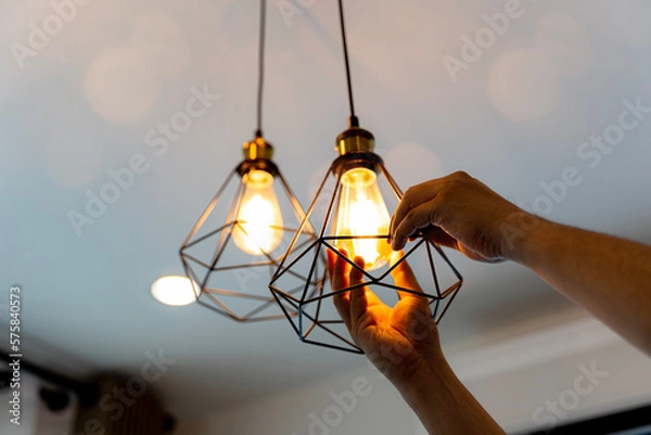 Fototapeta Decorative antique edison style filament light bulbs hanging. An electrician is installing spotlights on the ceiling