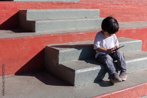 Fototapeta Mexican kid playing with smart phone outdoors