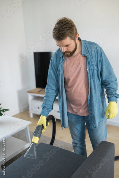 Fototapeta Man dry cleaner's employee hand in protective rubber glove cleaning sofa with professionally extraction method. Early spring regular cleanup. Commercial cleaning company concept