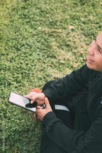 Fototapeta Smiling latino teenager looking at his smartphone screen