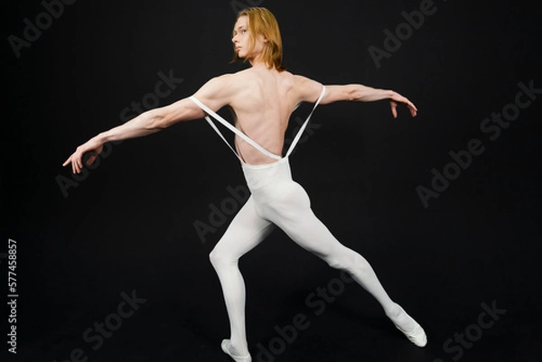 Fototapeta Young athletic professional ballet dancer with a bare torso and white dance tights is in perfect shape, performing and posing over a black background.