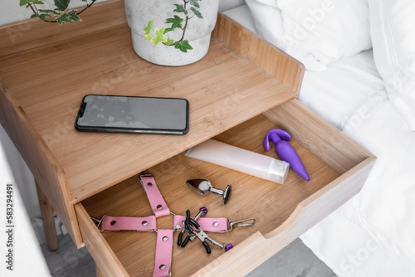 Fototapeta Open drawer with sex toys and mobile phone in bedroom