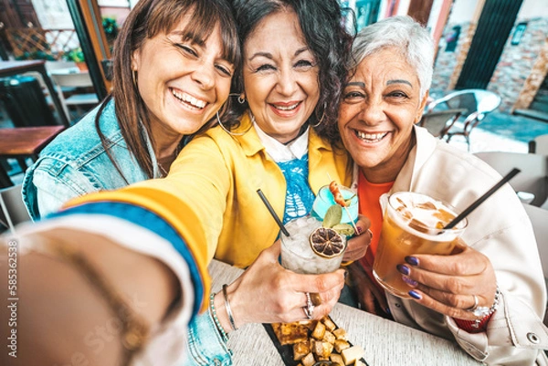 Fototapeta Happy senior women drinking cocktail glasses sitting at bar table - Group of best friends enjoying happy hour cheering drinks at pub restaurant - Life style concept with girls hanging out together