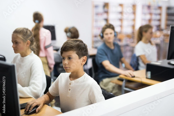 Fototapeta Preteen boy and girl learn to solve problems on computer in a school classroom