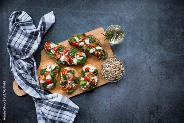 Fototapeta Bruschetta (sandwiches) with cherry tomatoes, mozzarella cheese and herbs on a cutting board on a dark background. Traditional Italian snack.