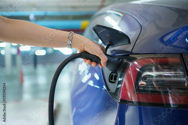 Fototapeta Beautiful Asian woman connecting a AC Type 2 EV charging connector to a vehicle, woman preparing an EV - electric vehicle charging connector for recharge a vehicle.