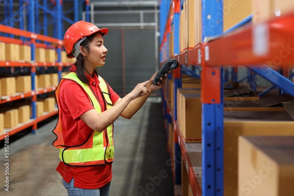 Fototapeta Warehouse workers woman with hardhats and reflective jackets scanning barcode on large box package for delivery to production stock and inventory in retail warehouse logistics, distribution center