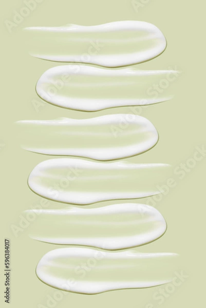 Obraz Lots of smears of cosmetic cream. Light, smooth surface.  In a row. At an angle. Top view. Texture of flowing cream. Liquid creamy strokes. On green background. Cosmetic background, banner.