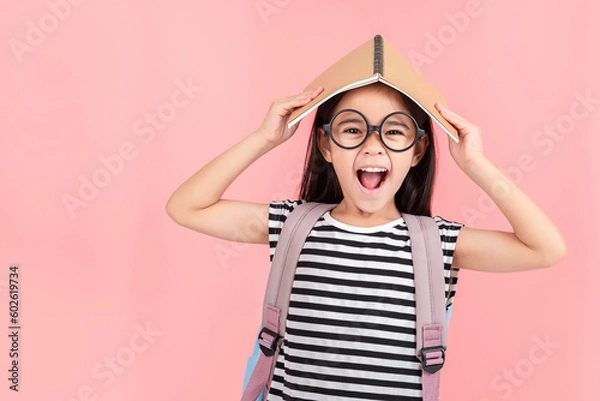 Fototapeta schoolgirl hugging book wearing backpack smiling isolated on pink background